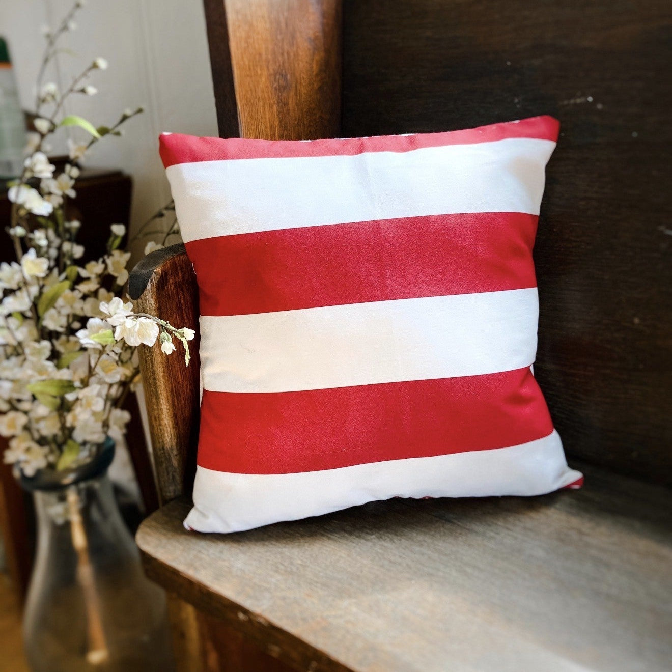 Red and white striped pillow on a wooden chair with a vase of flowers in the background.