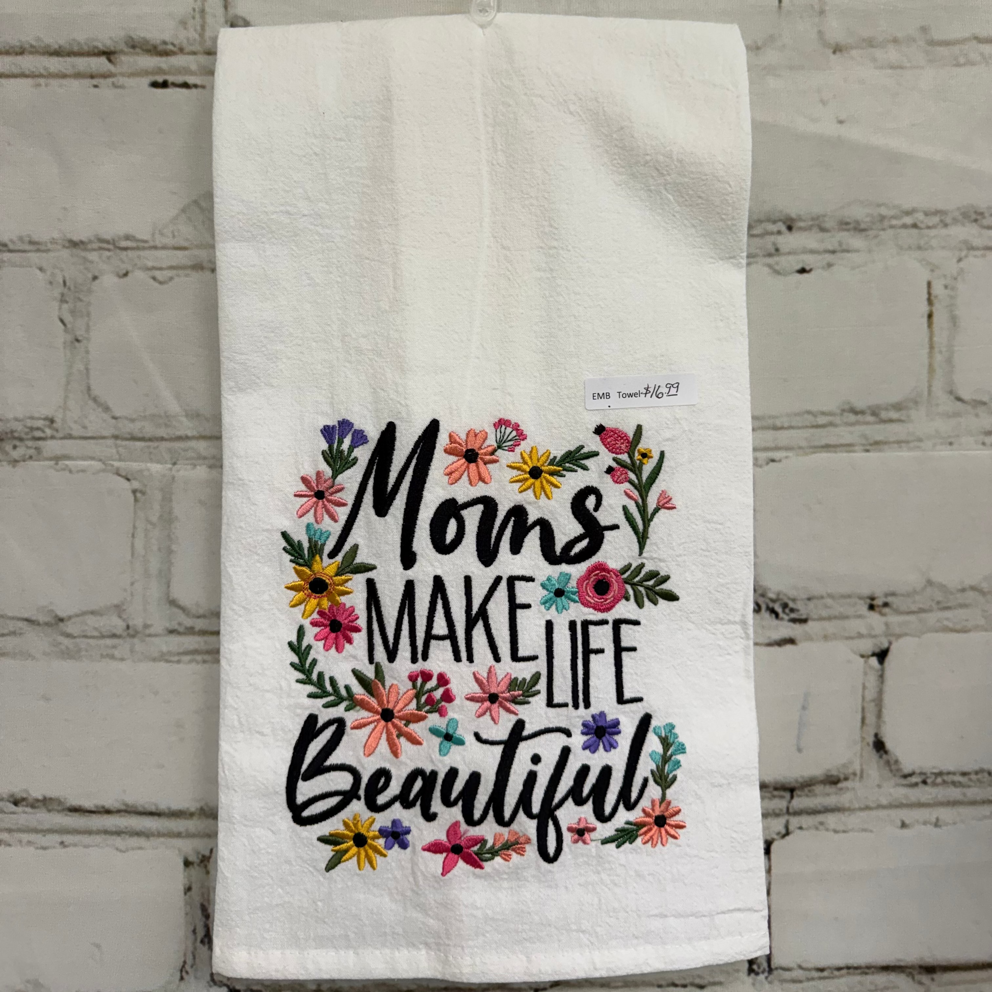 White towel with floral design and text hanging on a brick wall.