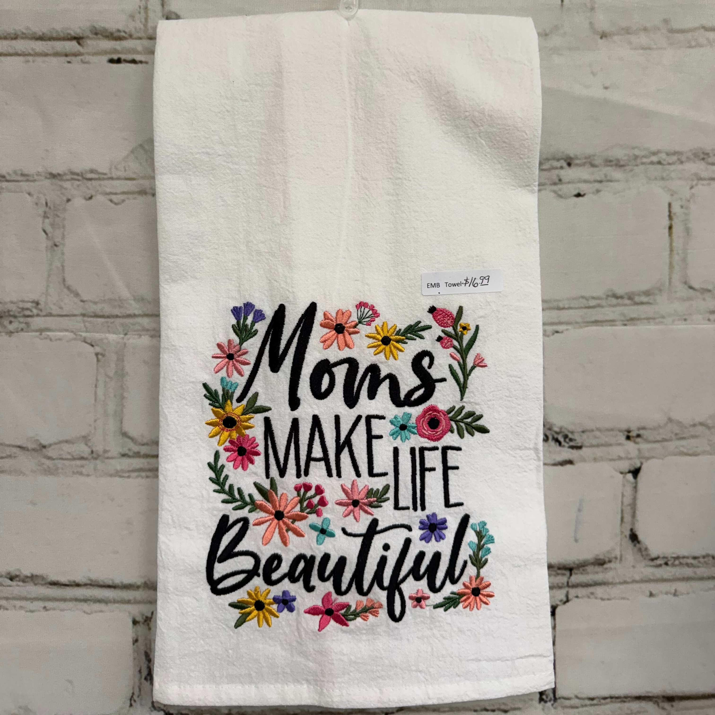 White towel with floral design and text hanging on a brick wall.