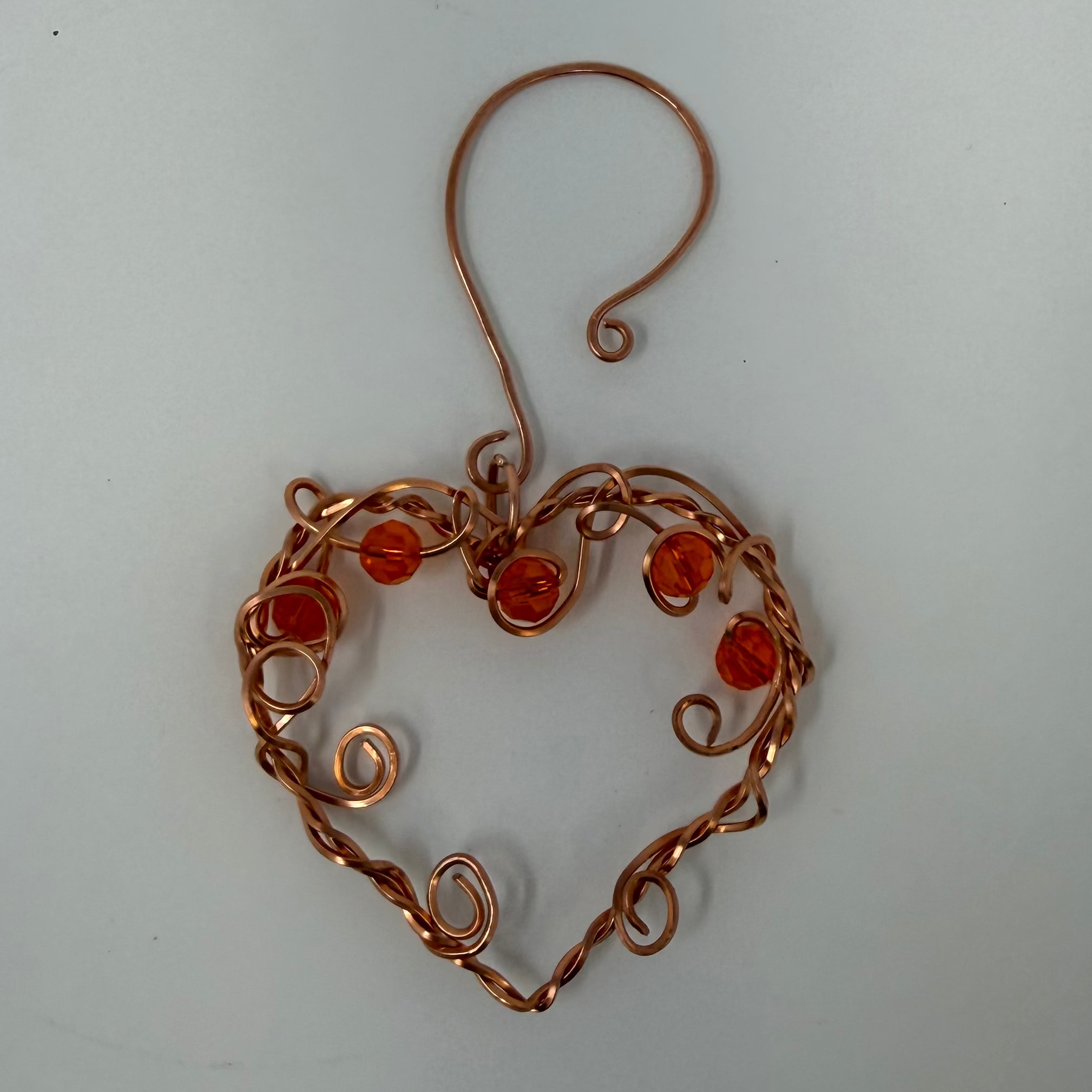 Copper heart-shaped earring with red beads on a light gray background