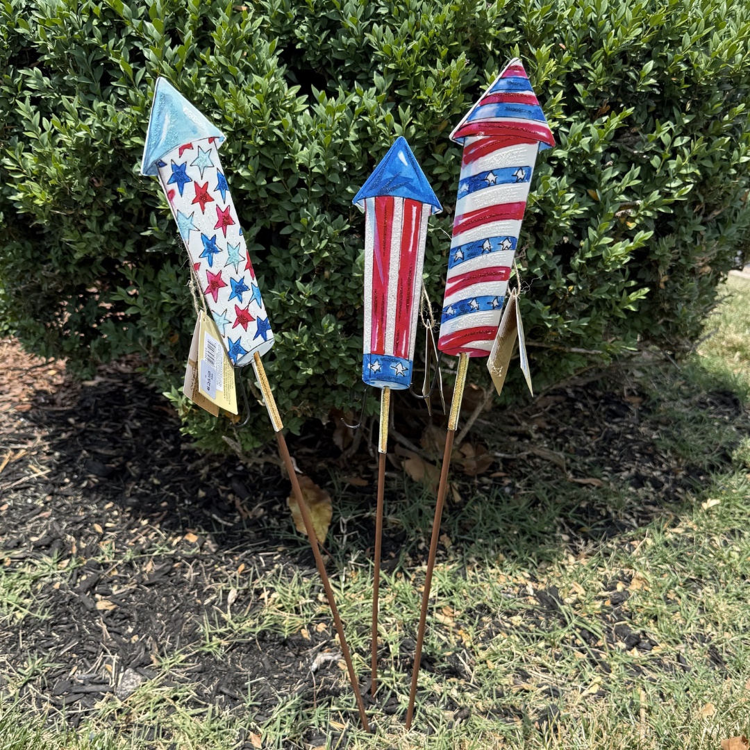 Decorative patriotic rocket-shaped stakes in a garden setting.