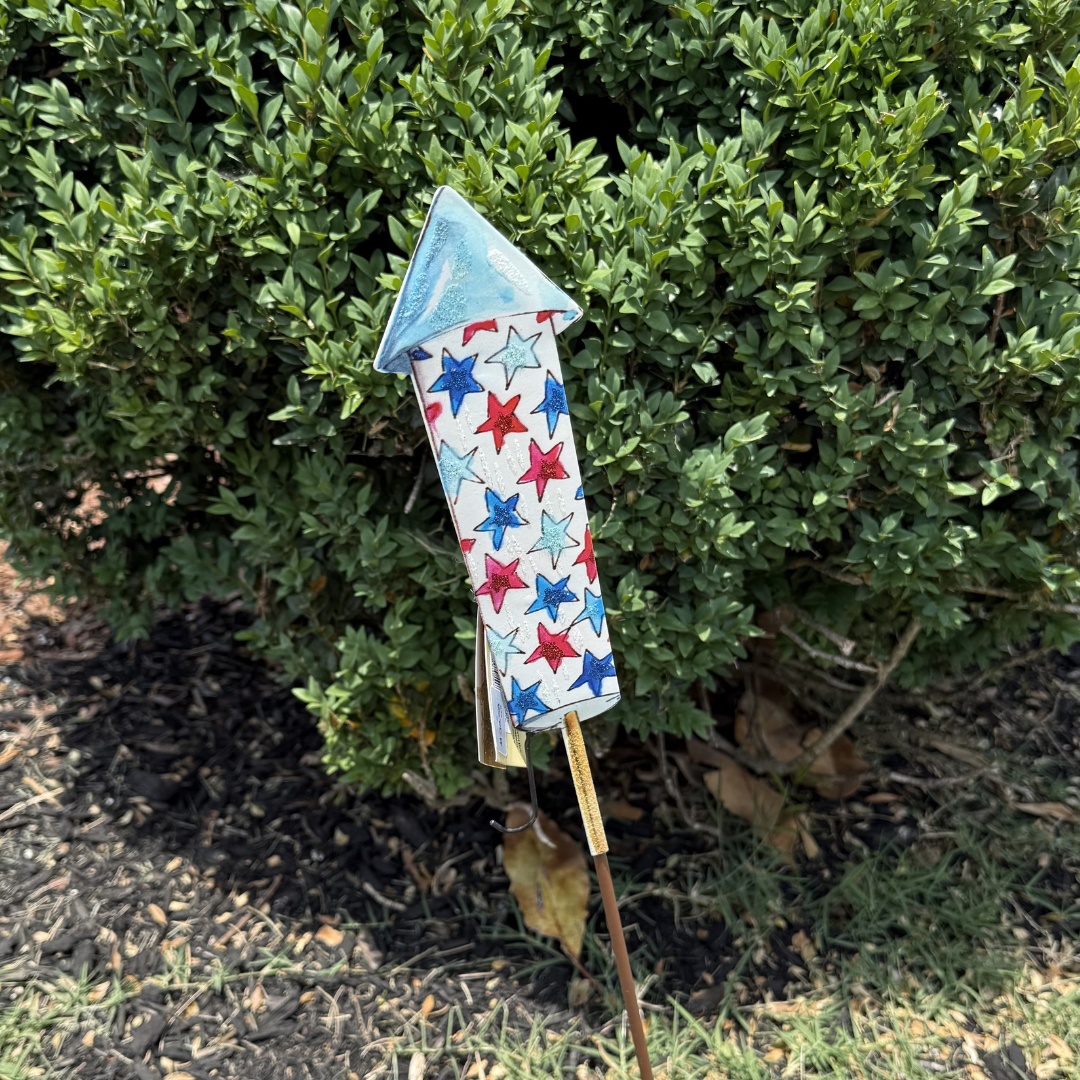 Decorative arrow with star pattern on a stick in front of green bushes