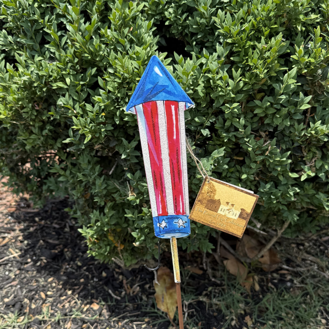 Decorative garden stake with American flag design against a green bush background
